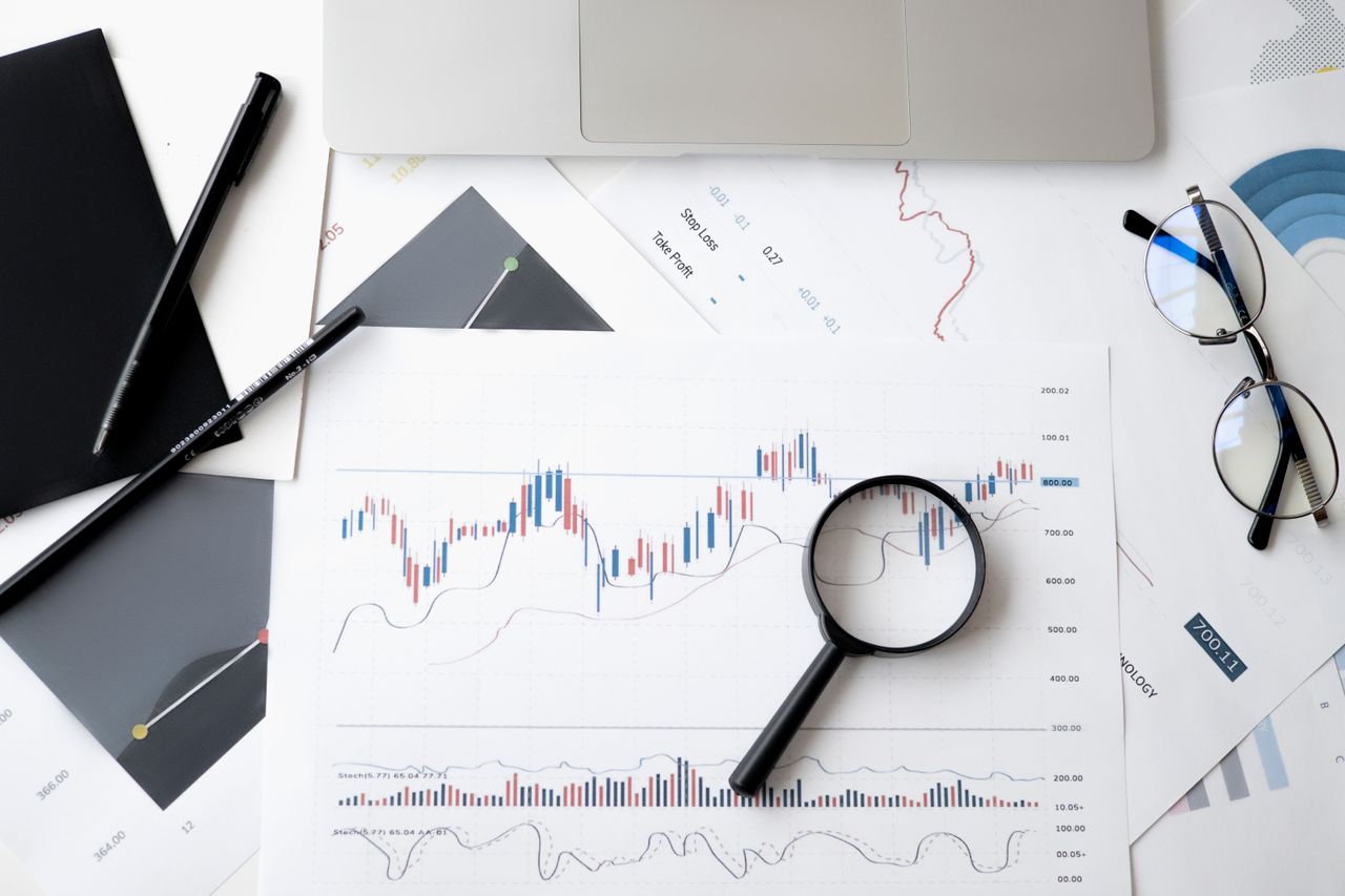 services-01 Flat lay of stock market analysis documents with magnifying glass, pens, and glasses.